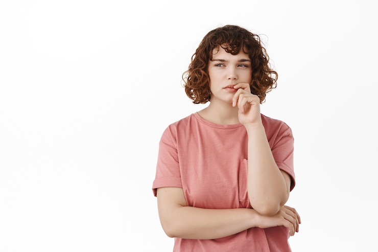Foto chica rizada pensativa, mirando a un lado con rostro serio pensativo, pensando, haciendo suposiciones, de pie en camiseta en blanco