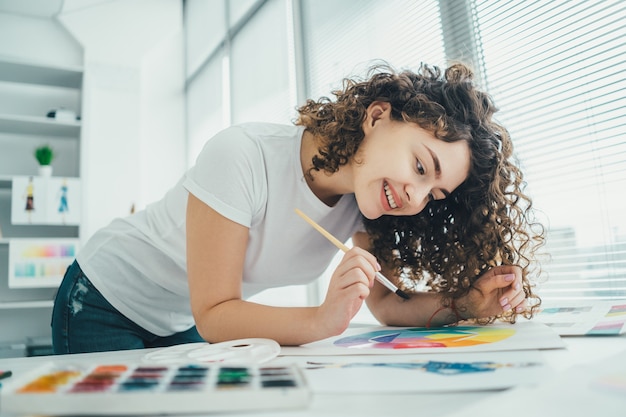 La chica rizada pintando un cuadro en la mesa.