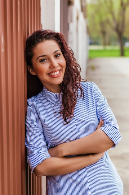 Foto chica rizada posando mientras está de pie junto a la pared exterior