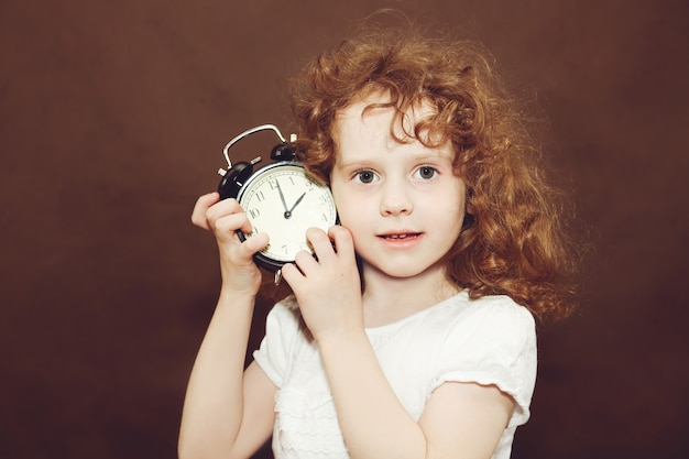 Foto chica rizada con reloj despertador. foto en tonos marrones.