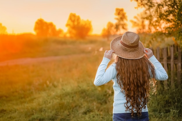 Chica rizada en un sombrero de paja descansando en la puesta de sol de verano al aire libre Concepto de vacaciones