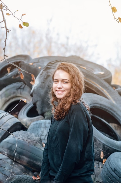 Chica rizada con una sonrisa radiante en el fondo de un montón de neumáticos Problemas ecológicos