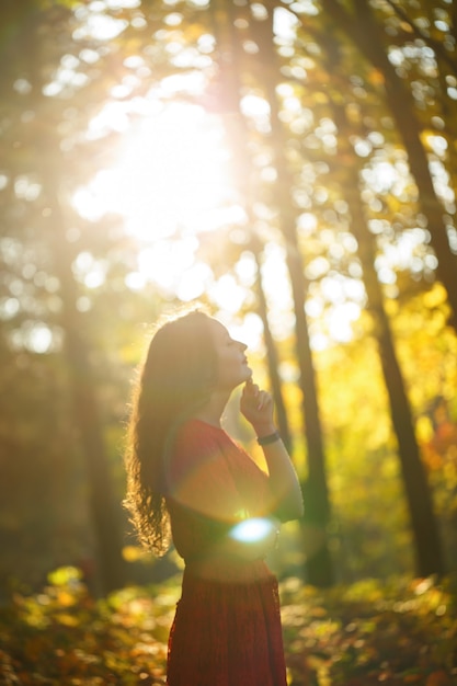 Chica con rizos en un vestido rojo en el bosque de otoño