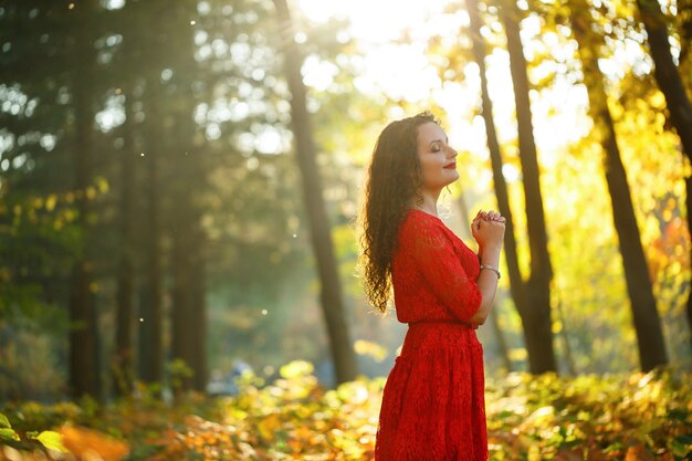 Chica con rizos en un vestido rojo en el bosque de otoño