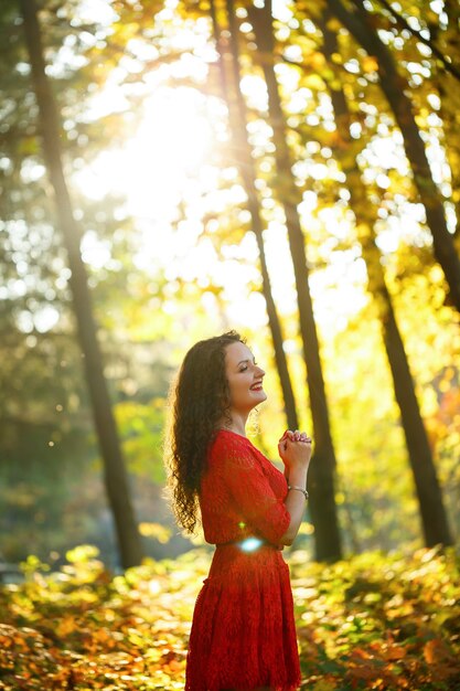 Chica con rizos en un vestido rojo en el bosque de otoño