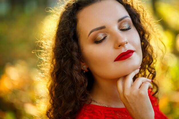 Chica con rizos en un vestido rojo en el bosque de otoño