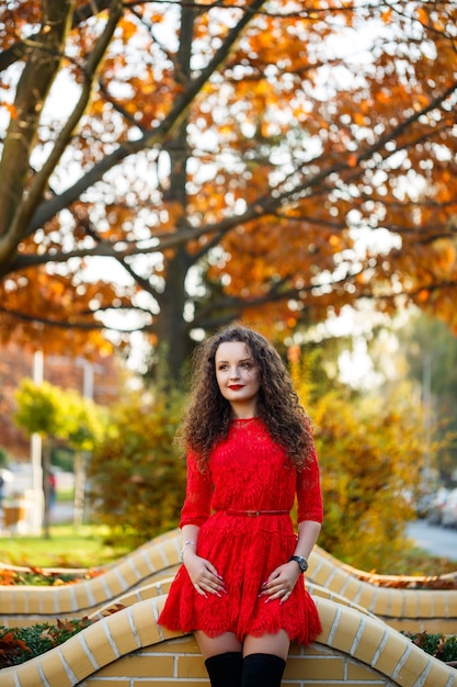 Chica con rizos en un vestido rojo en un callejón de la ciudad de otoño