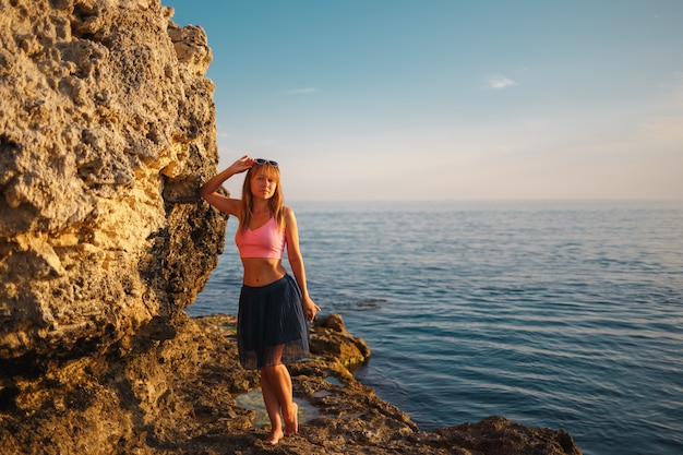 Chica en las rocas en el mar al día del atardecer