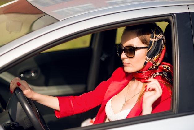 Chica en rojo y gafas de sol conduciendo un coche. mujer de negocios en un auto, con gafas de sol