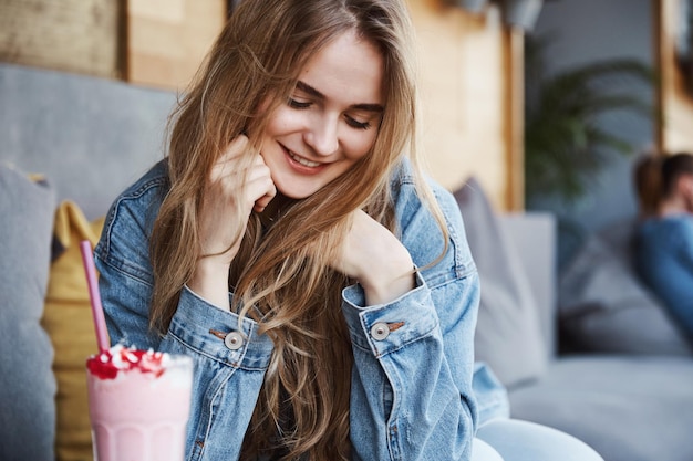 Chica romántica sentada en el café y sonrojándose bebiendo fresa