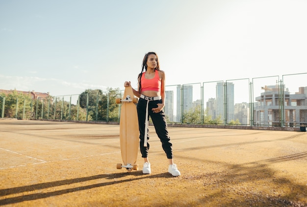 Chica en ropa de calle de moda se encuentra con un longboard