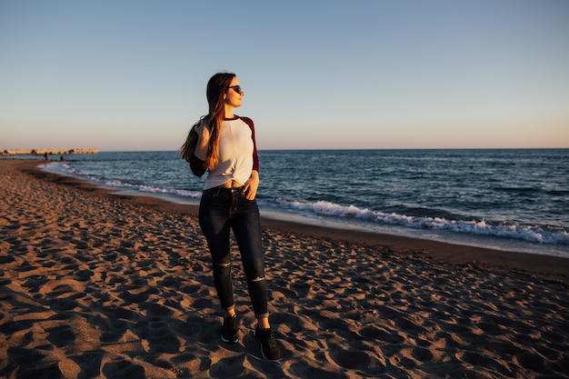 Chica en ropa casual con gafas de pie en una playa del mar Mediterráneo