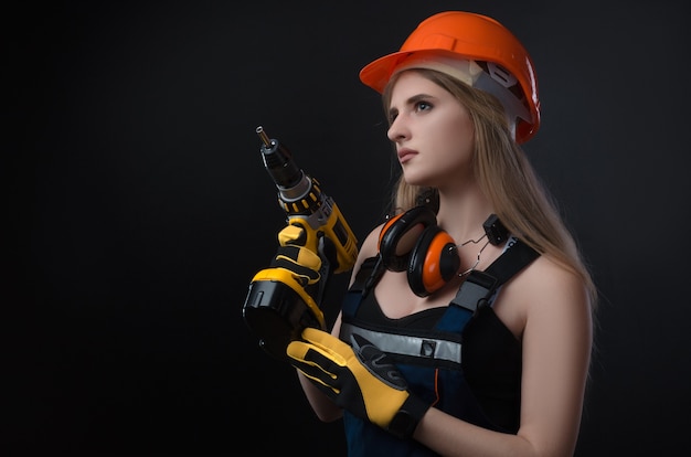 La chica en ropa de construcción y equipo de protección posando con un destornillador