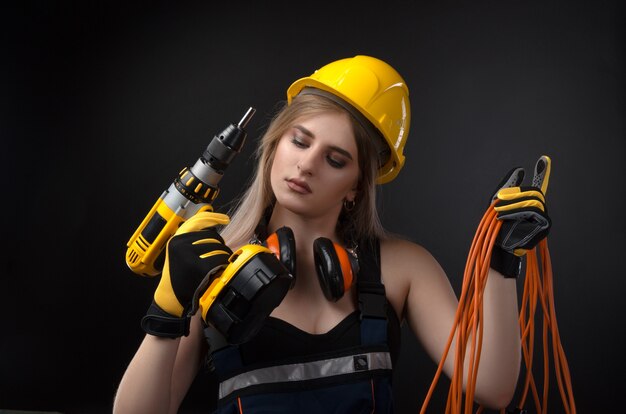 La chica en ropa de construcción y equipo de protección posando con un destornillador