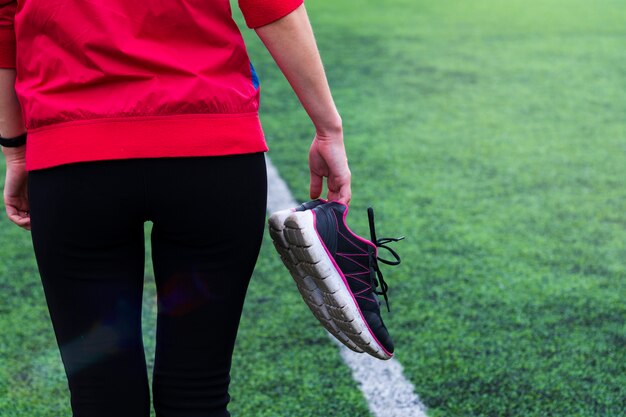 La chica en ropa deportiva camina por el estadio y lleva zapatillas en sus manos.