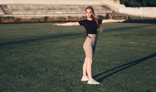 Chica en ropa deportiva extendió sus brazos a los lados en el estadio