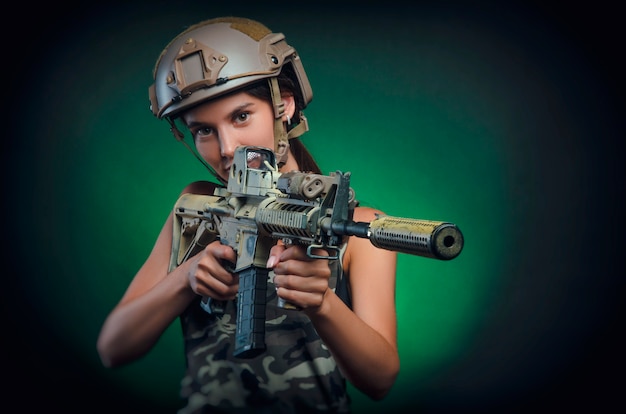 La chica en ropa especial militar posando con una pistola en sus manos sobre un fondo oscuro en la bruma