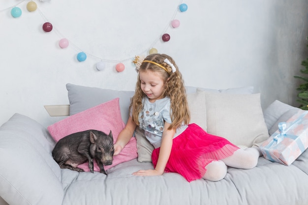 Chica en ropa festiva y mini cerdo. Símbolo de cerdo de 2019. Cerdo negro como symbil para 2019 en horóscopo chino. Mascota y niño Amistad y cuidado de los más pequeños.