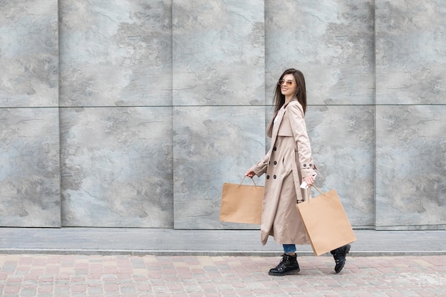 Una chica con ropa informal con bolsas de compras y muchas compras cerca del centro comercial, sonriendo, le entrega su paquete, venta de consumismo y concepto de personas.