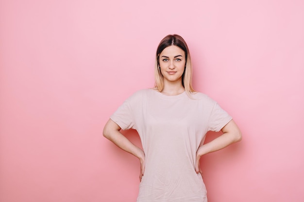 La chica con ropa informal se para con las manos en las caderas y mira a la cámara. El cabello está peinado hacia atrás.