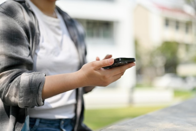 Una chica con ropa informal usando su teléfono inteligente mientras se relaja en un parque público