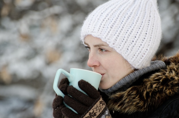 Chica en ropa de invierno bebiendo té de una taza, vista lateral, primer plano