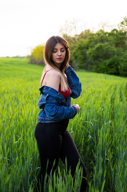 Una chica en ropa de mezclilla con un cabello hermoso se encuentra en un campo verde