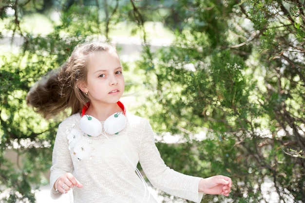 Chica en ropa de moda sobre fondo natural. Niño con pelo largo y rubio al aire libre. Kid modelo en vestido de moda. Moda, estilo y tendencia. Infancia y puericultura.