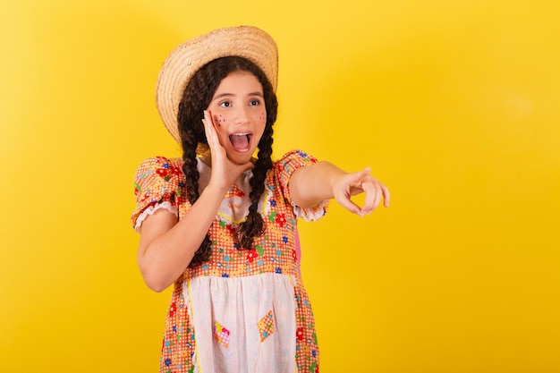 Chica con ropa naranja tradicional para festa junina Avistamiento y señalando algo lejano increíble Anuncio de promoción