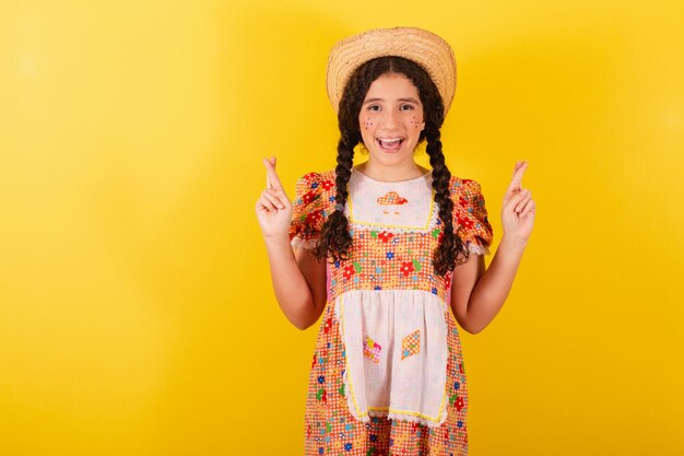 Chica con ropa naranja tradicional para festa junina Dedos cruzados signo de suerte buena suerte animando