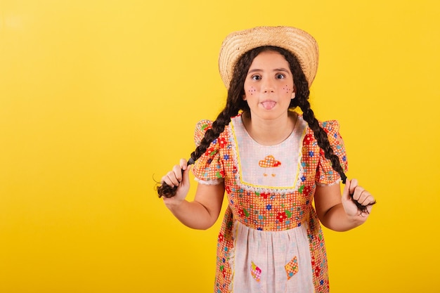 Chica con ropa naranja tradicional para festa junina Sosteniendo trenzas de cabello Haciendo muecas