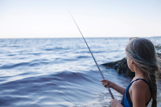 Chica en ropa de natación pesca desde la playa del mar en las primeras horas de la mañana blue hours active weekend camping