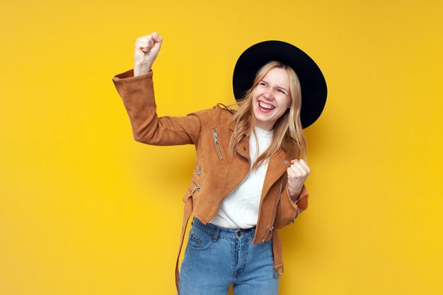 Chica en ropa de otoño se regocija en la victoria sobre un fondo amarillo aislado hermosa mujer gana