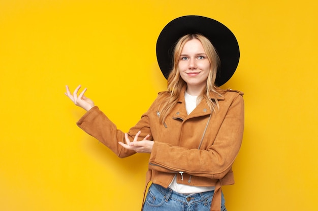 Chica con ropa de otoño y un sombrero sonríe y muestra con las manos a un lado en copyspace