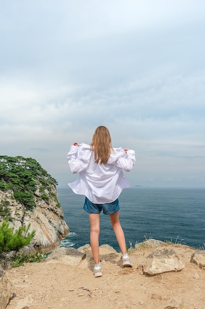 Chica con ropa de verano en la cima de la montaña cerca del mar