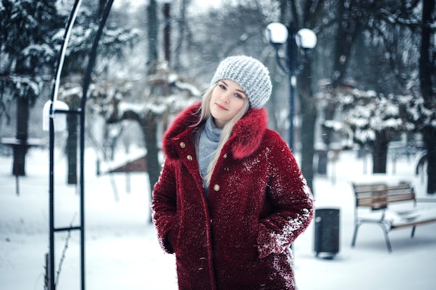 Chica rubia en abrigo rojo en el parque cubierto de nieve