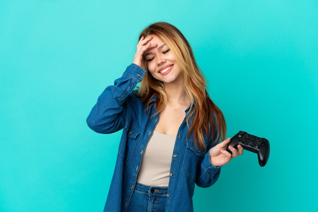 Chica rubia adolescente jugando con un controlador de videojuegos sobre pared aislada sonriendo mucho