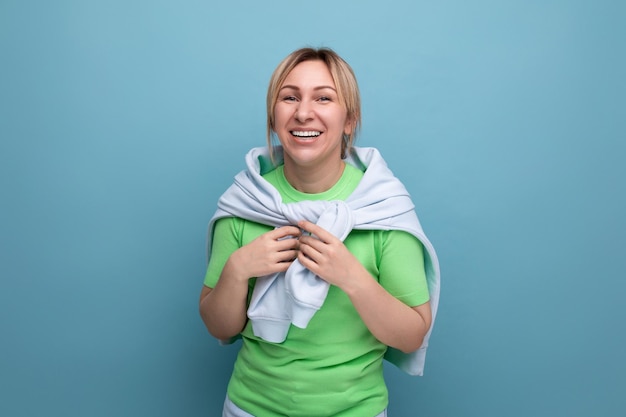 Una chica rubia alegre y sonriente con un atuendo informal sonríe ampliamente en un fondo azul con copia