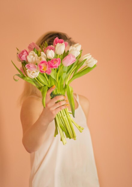 Chica rubia alegre sosteniendo un ramo de tulipanes sobre fondo beige Retrato de una joven feliz con ropa informal tomando un ramo de tulipanes