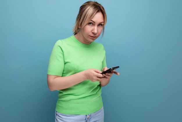 Chica rubia atractiva medita sosteniendo un teléfono inteligente en la mano sobre un fondo azul con copia