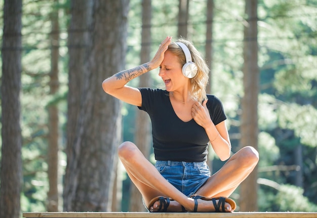 Chica rubia con auriculares está gritando poniendo la mano en la frente en el fondo de la naturaleza