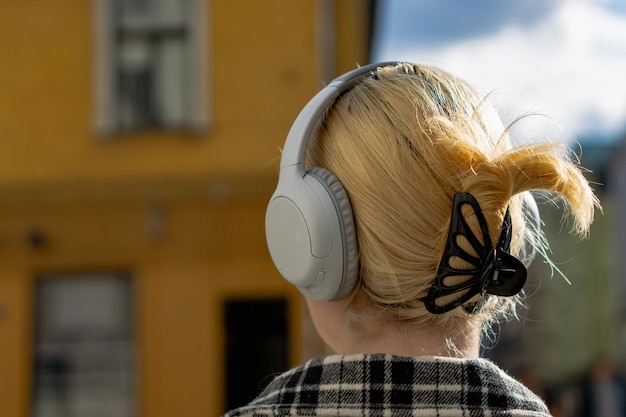 Chica rubia con auriculares inalámbricos en la calle en un día soleado de verano Vista desde atrás