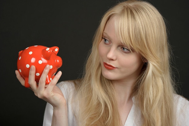 Chica rubia con caja de ahorros alcancía roja