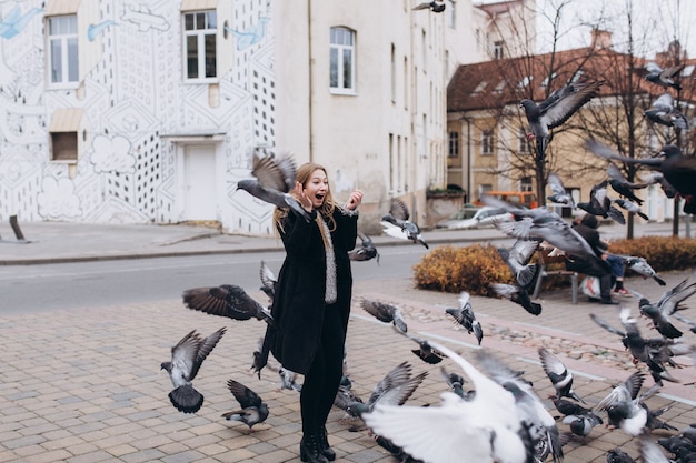 Chica rubia en la calle de la ciudad con palomas volando