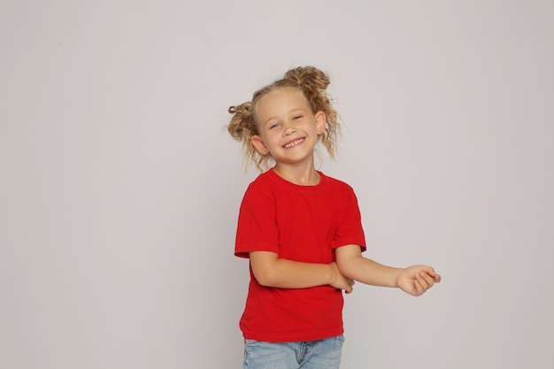 una chica rubia con una camiseta roja y jeans con coletas muestra emociones