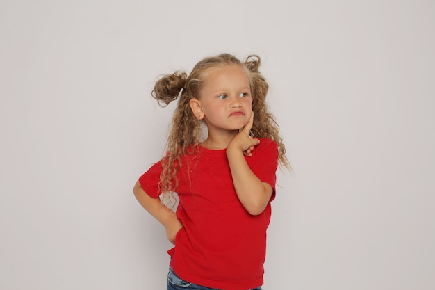 una chica rubia con una camiseta roja y jeans con coletas muestra emociones