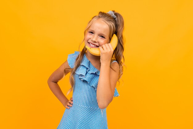 Chica rubia caucásica hablando en un plátano como en el teléfono en una pared amarilla