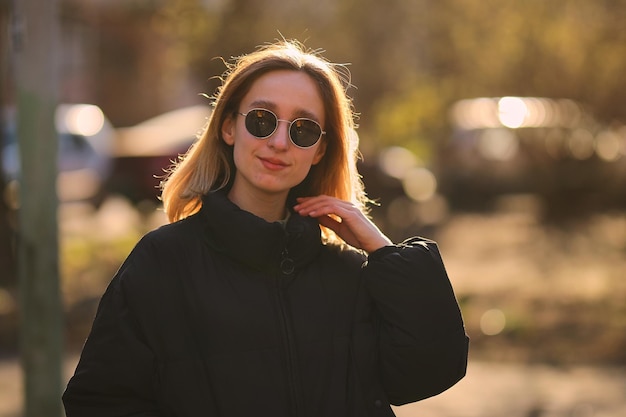 Una chica rubia con una chaqueta negra y gafas de sol negras camina por la calle