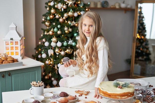 chica rubia en la cocina de año nuevo con pastelitos y dulces