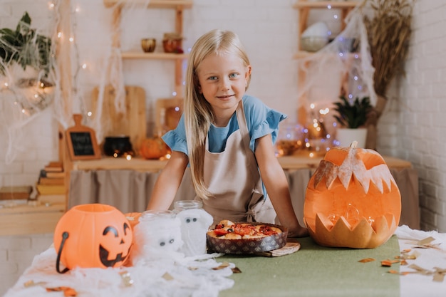 Chica rubia en delantal en la cocina decorada con calabazas para Halloween prepara un pastel de focaccia